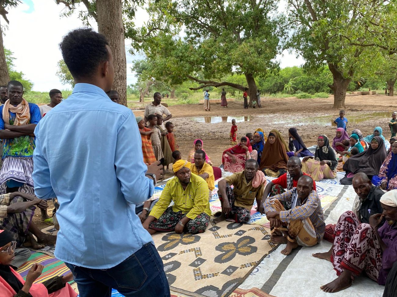 A KPHF officer leading a community dialogue with men and women seated under trees